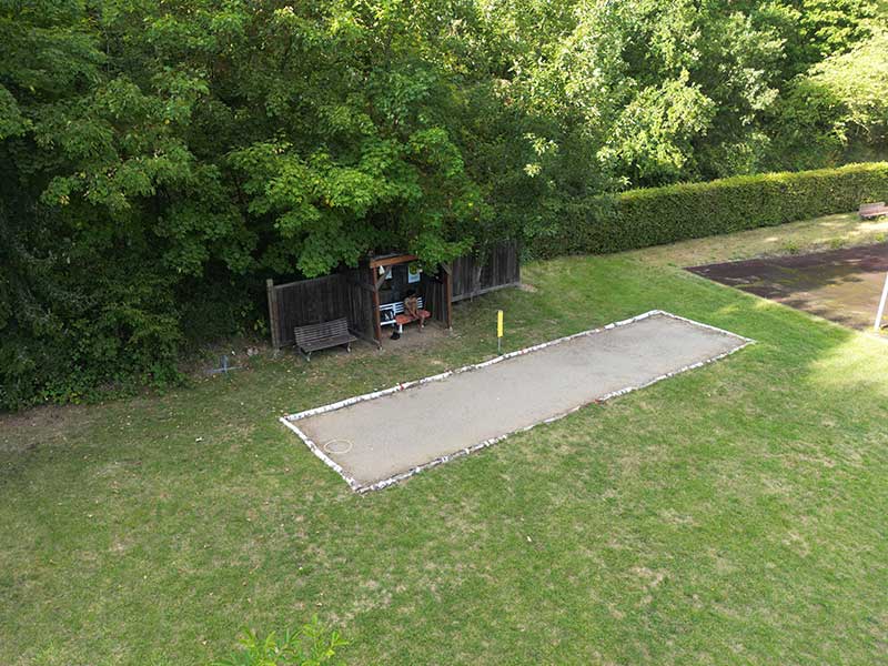 Ein rechteckiger Boccia-Platz auf Rasen in der Nähe von Bäumen in Zieselsmaar, im Hintergrund ein kleiner Holzunterstand und eine Bank.