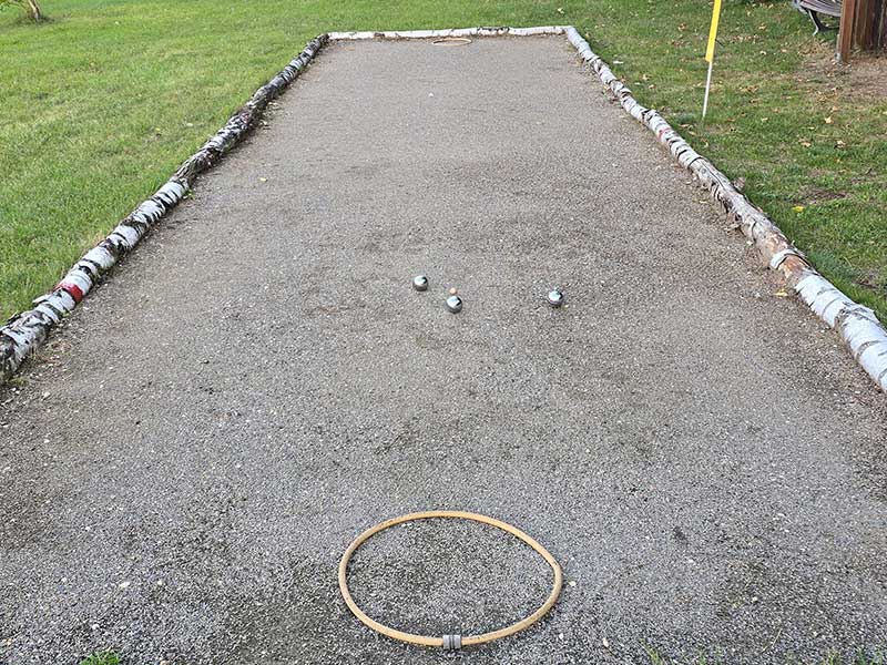 Ein Boccia-Platz mit drei silbernen Kugeln auf Kies und einem Holzring an einem Ende lädt zu einem einzigartigen textilfreien Sporterlebnis ein.