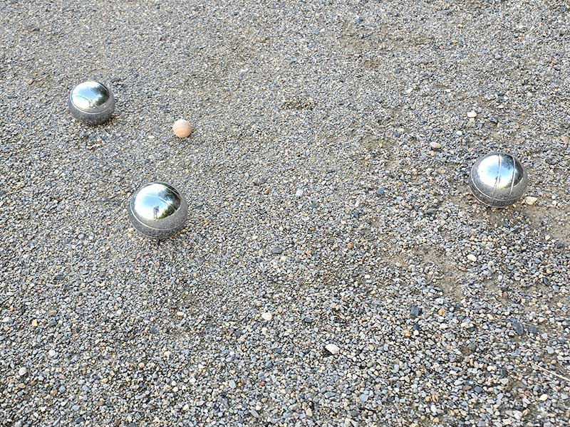 Drei metallene Pétanque-Kugeln und eine kleine Holzkugel liegen auf dem Kiesboden in Zieselsmaar, einem beliebten Treffpunkt für FKK- und Textilfrei-Fans.