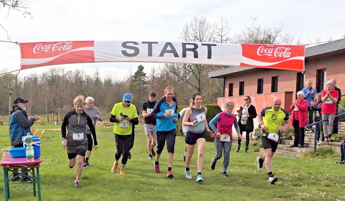 Eine Gruppe von Läufern startet ein Rennen unter einem Banner mit der Aufschrift „START“, an dessen beiden Enden Coca-Cola-Logos zu sehen sind – ein Symbol für den Freizeitgeist in Zieselsmaar.