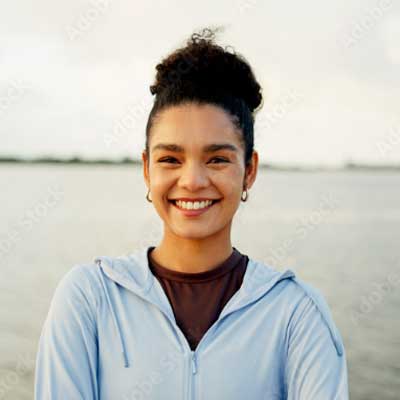Eine lächelnde Frau in einer hellblauen Jacke steht an einem bewölkten Tag am Wasser in Zieselsmaar und genießt ihre Freizeit.