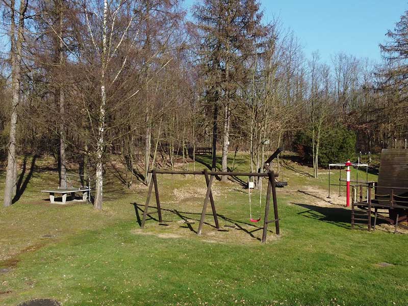 Ein Spielplatz mit Schaukeln, einer Bank und Spielgeräten, umgeben von Bäumen in Zieselsmaar, ist an einem sonnigen Tag der perfekte Ort für Freizeitaktivitäten.