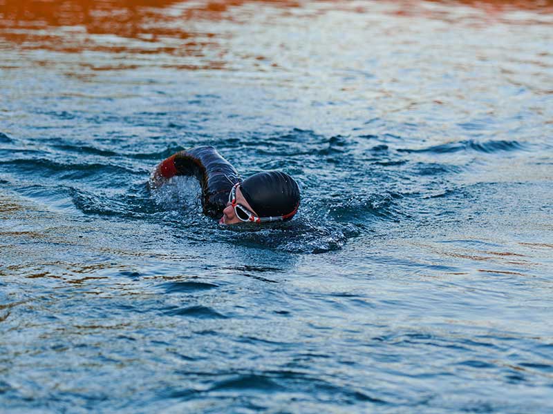 Eine Person, die in Zieselsmaar Freizeitsport betreibt, trägt eine Schwimmbrille und eine Badekappe und schwimmt im Freistil im offenen Wasser, umgeben von sanften Wellen.