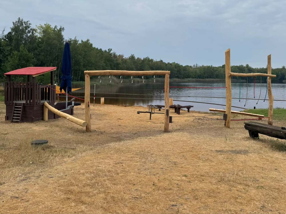 Ein Spielplatz mit Schaukeln, einer Bank und Spielgeräten, umgeben von Bäumen am Zieselsmaar, ist an einem sonnigen Tag der perfekte Ort für Freizeitaktivitäten.